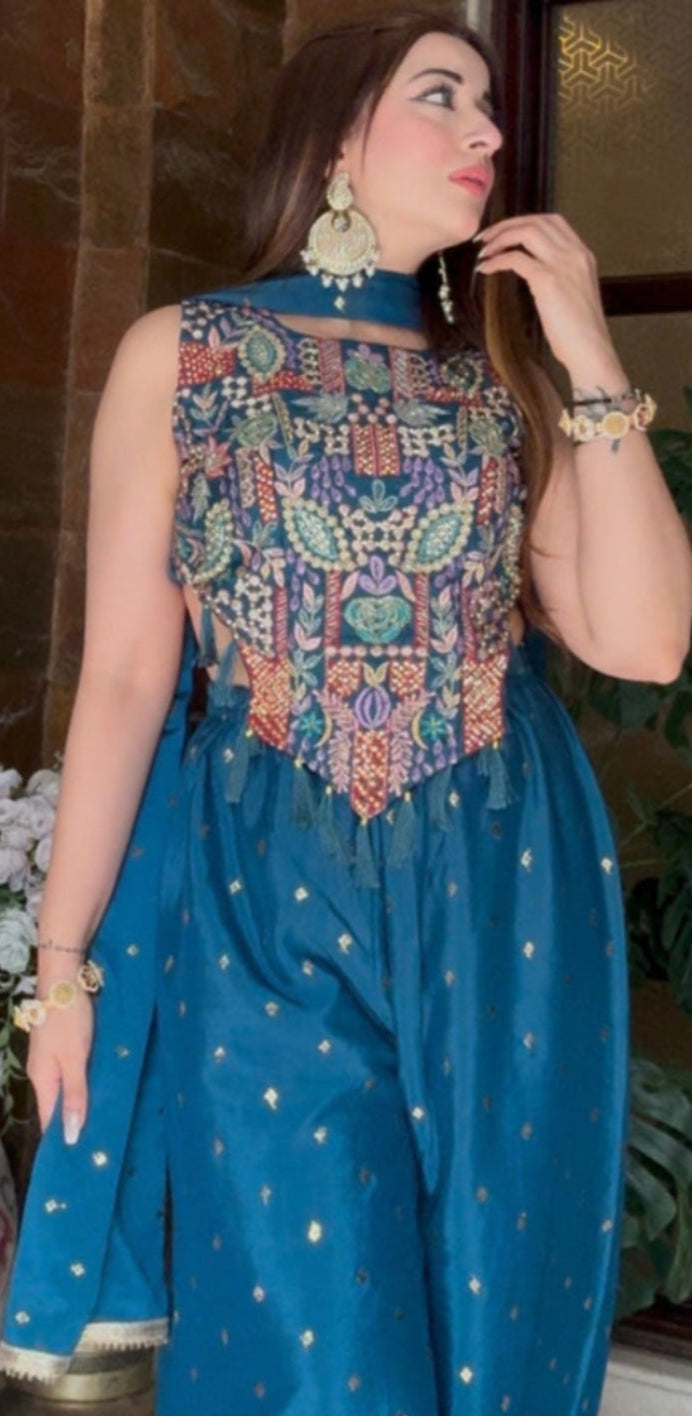Woman in a blue traditional outfit standing indoors with decorative elements.