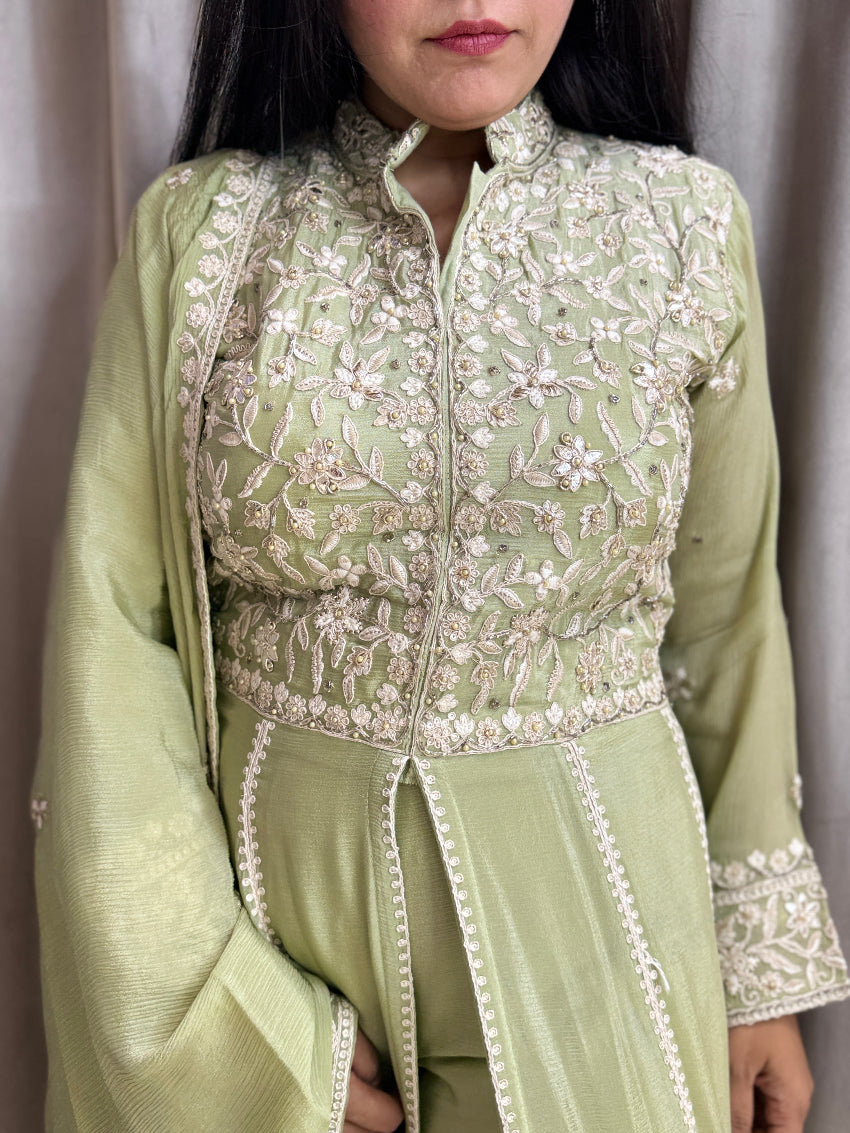 Person wearing a light green traditional outfit with floral embroidery against a neutral background