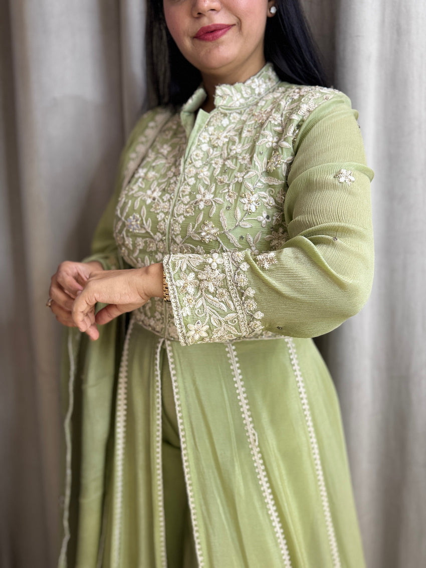 Woman wearing a light green traditional outfit with intricate white embroidery against a neutral background