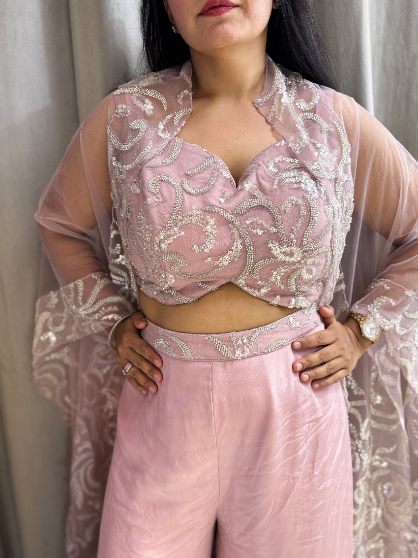 Person wearing a pink embroidered outfit with sheer sleeves against a neutral background