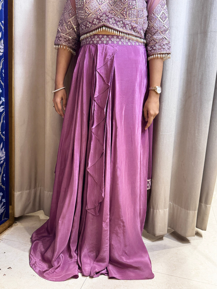 Person wearing a traditional outfit with a purple skirt and patterned top against a neutral background.