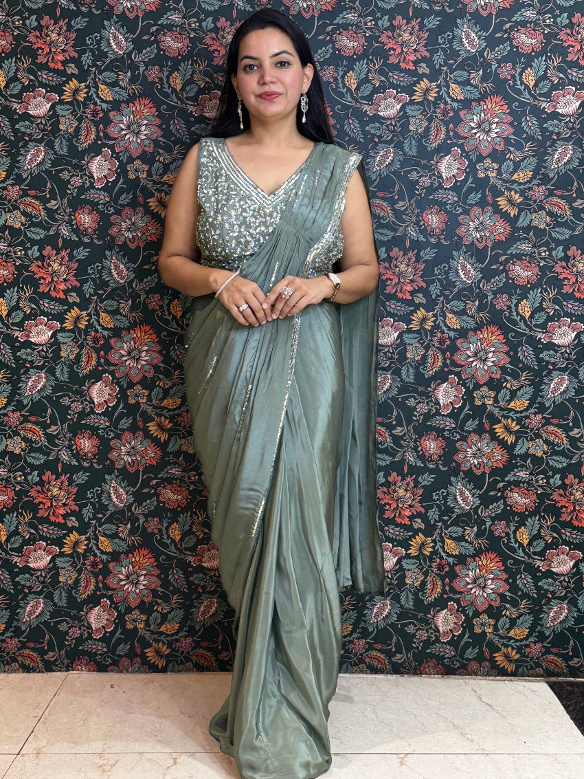 Woman in a silver saree standing against a floral-patterned wall.