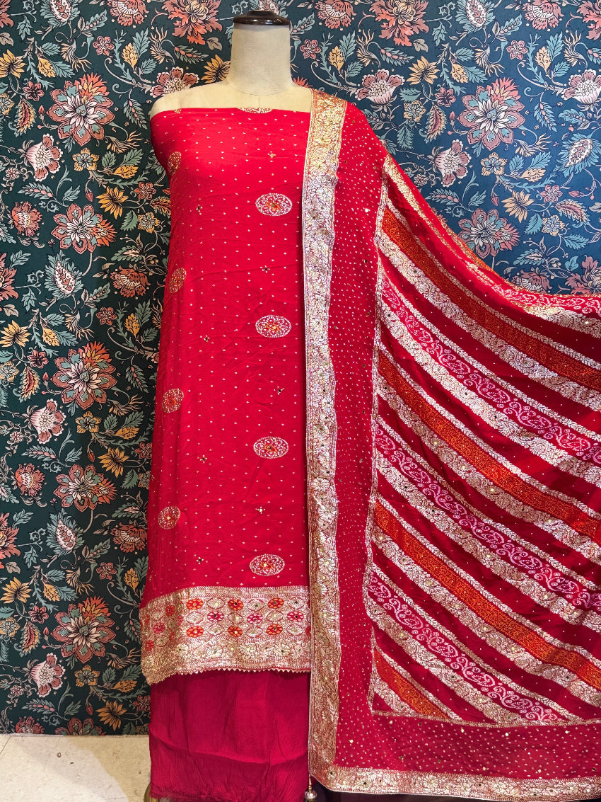 Red fabric with intricate patterns on a mannequin against a floral wallpaper background