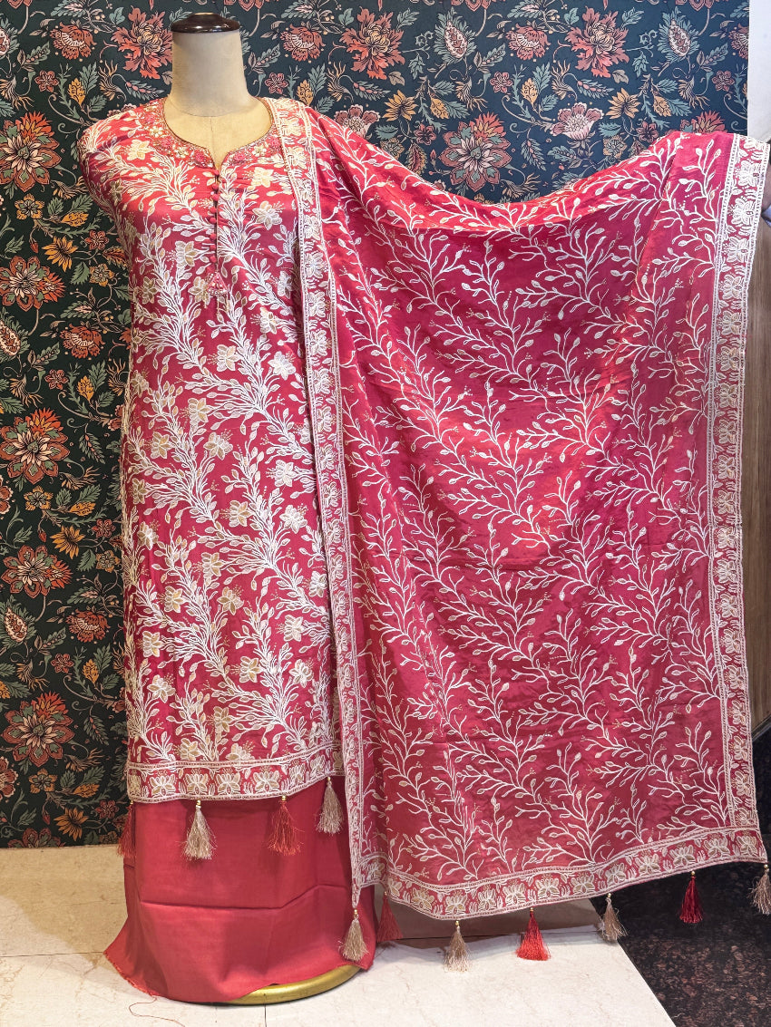 Pink saree with white floral patterns on a mannequin against a floral wallpapered wall.