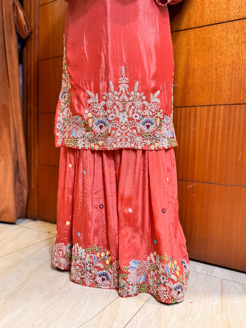 Red traditional outfit with floral embroidery on a wooden floor.