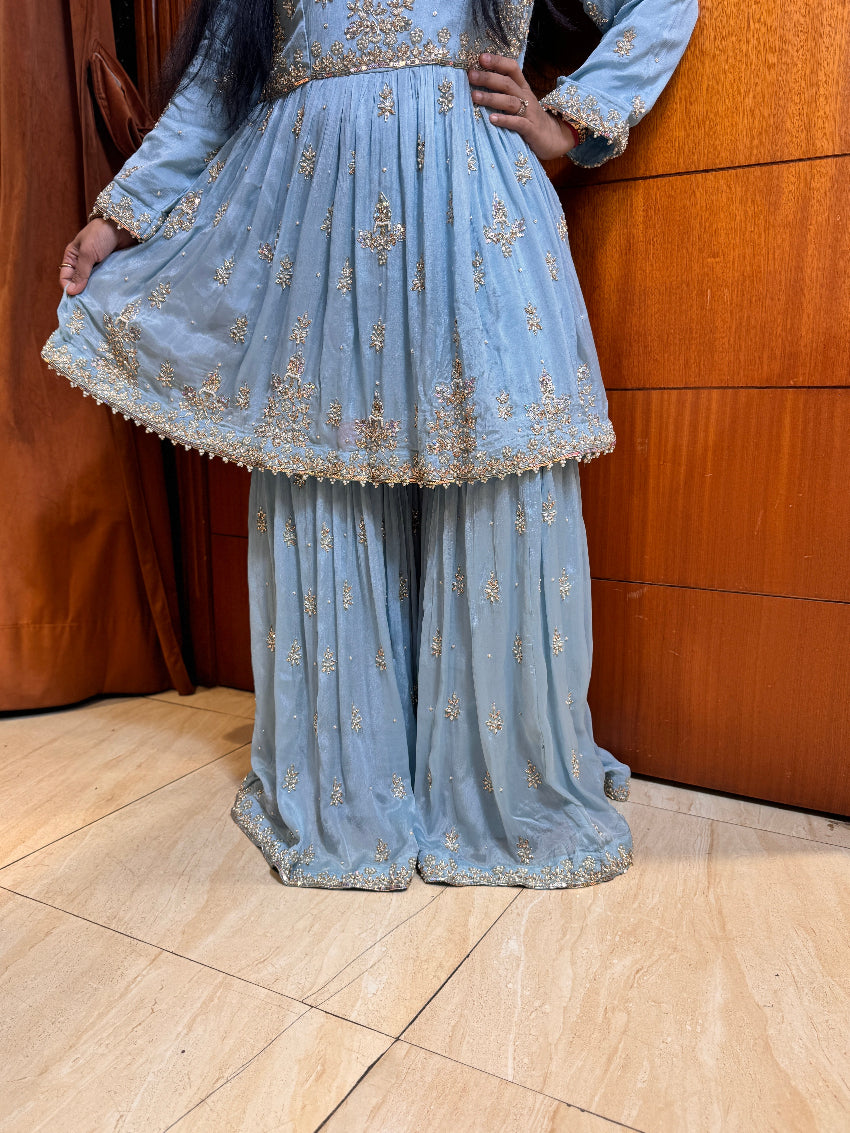 Light blue embroidered traditional outfit with gold details on a wooden floor.