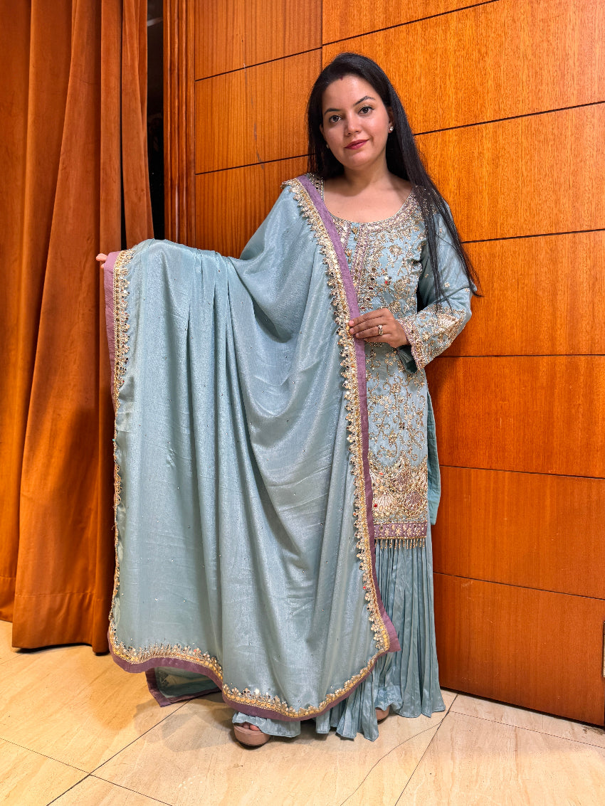 Woman in a light blue traditional outfit with a matching dupatta against a wooden panel background
