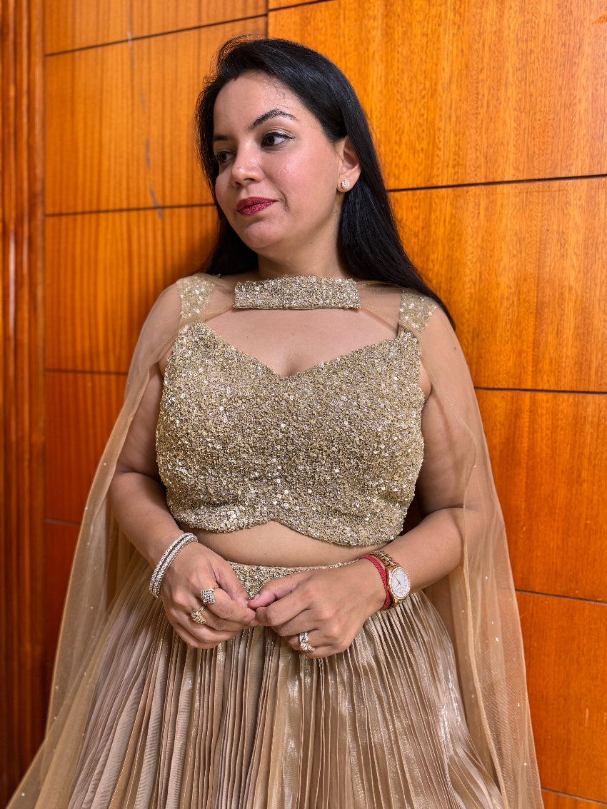 Woman wearing a gold sequin top and beige skirt against a wooden paneled wall.