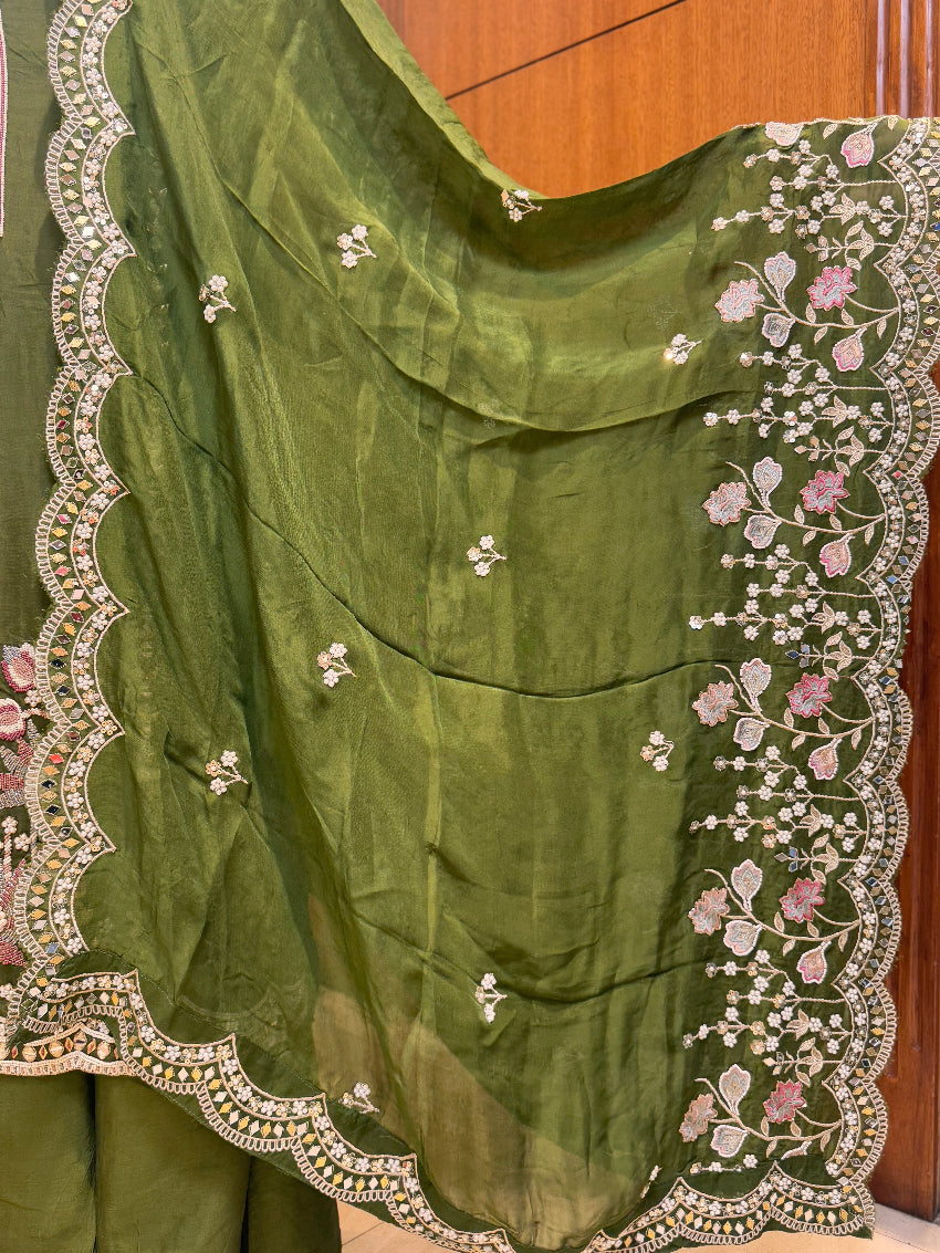 Green fabric with intricate white and pink floral embroidery on a wooden surface