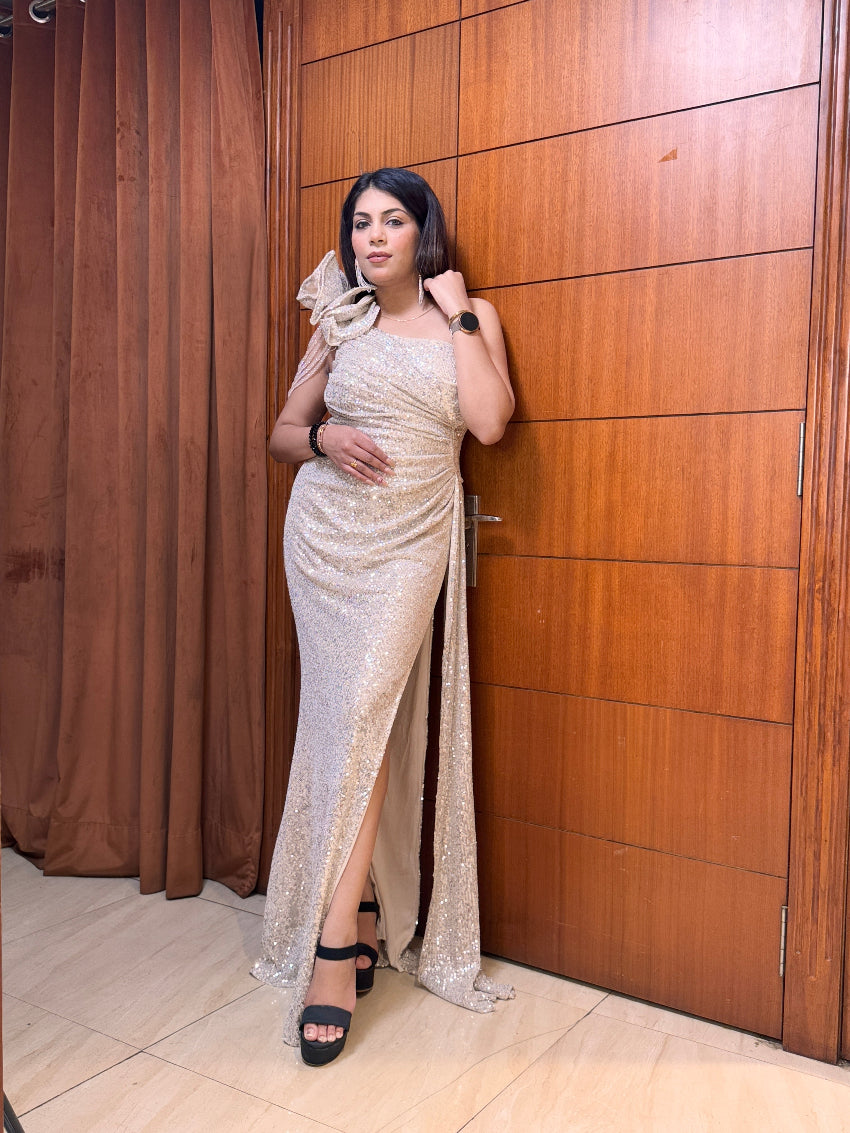 Woman in a silver evening gown standing against a wooden wall.
