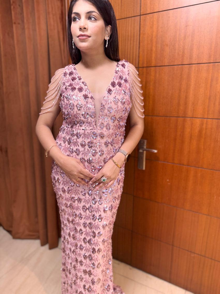 Woman in a pink floral dress standing in front of a wooden door.