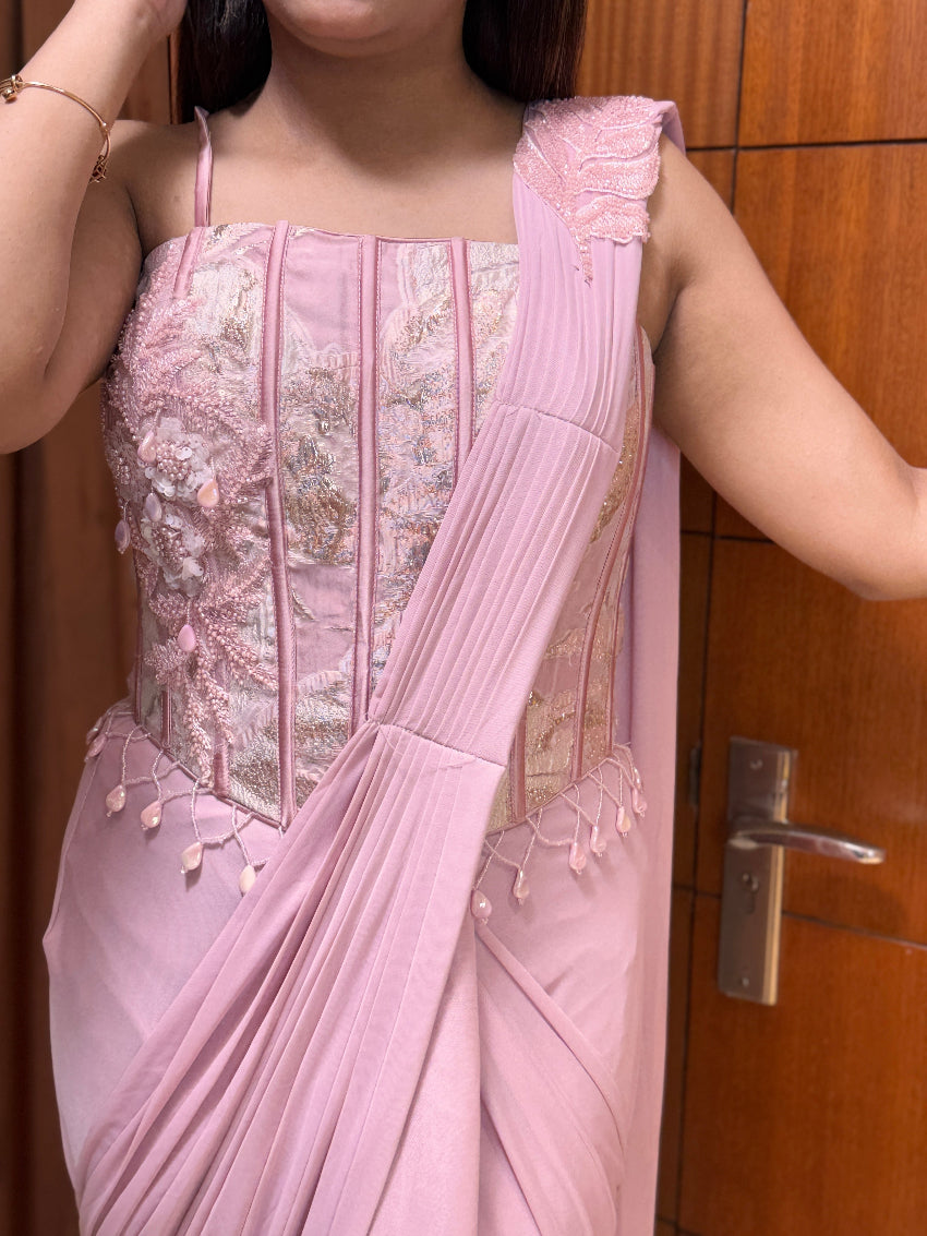 Person wearing a pink saree with intricate designs in front of a wooden door.