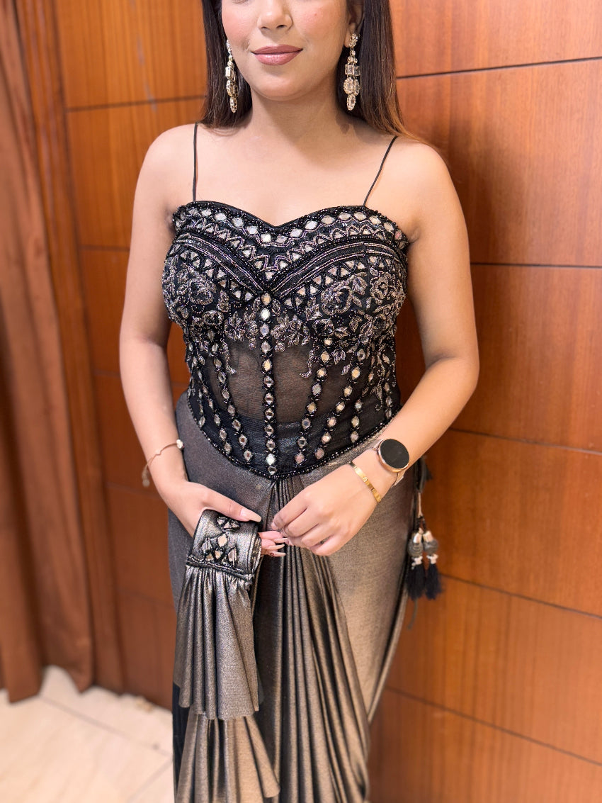 Woman wearing a black lace top and gray skirt against a wooden paneled wall.