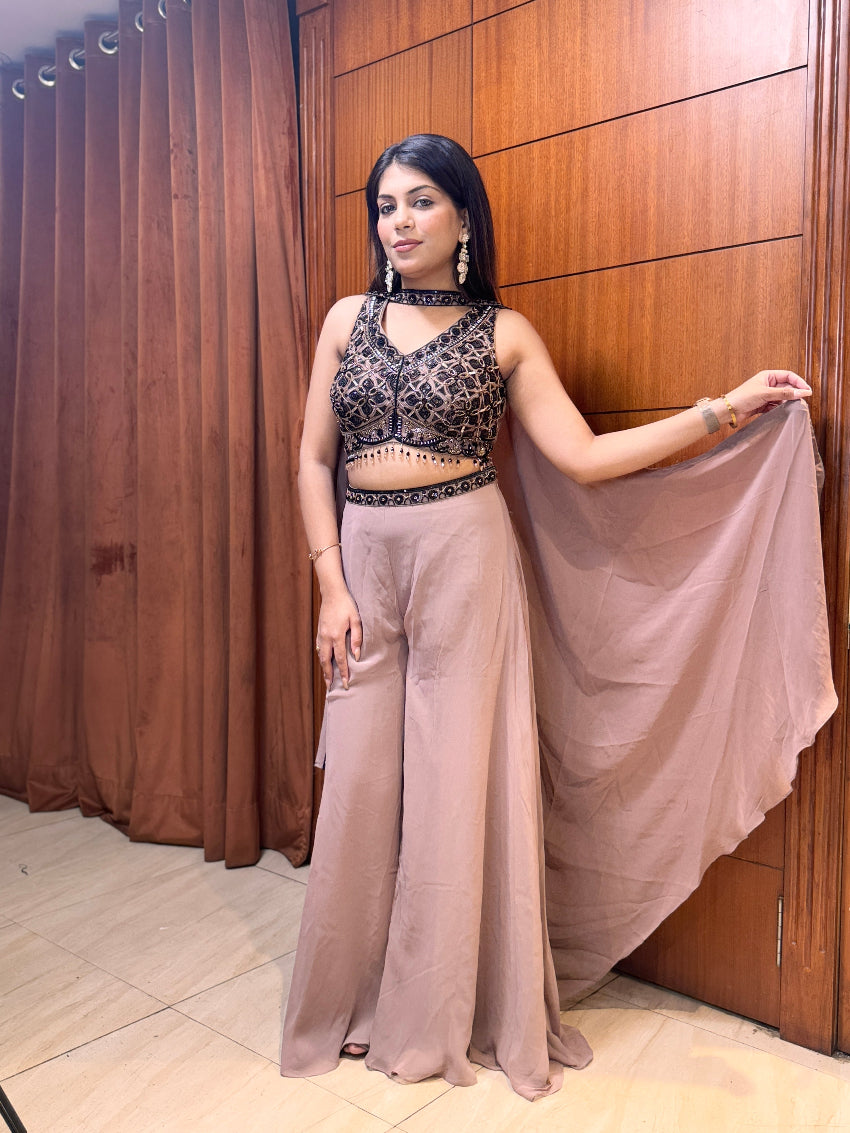 Woman in a black and beige traditional outfit standing against a wooden paneled wall.