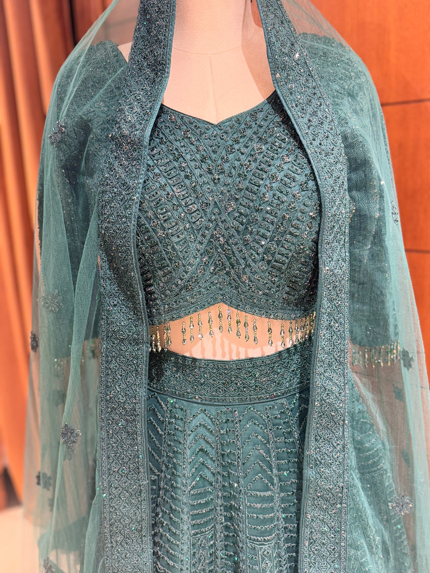 Green embroidered outfit with a sheer overlay on a wooden background