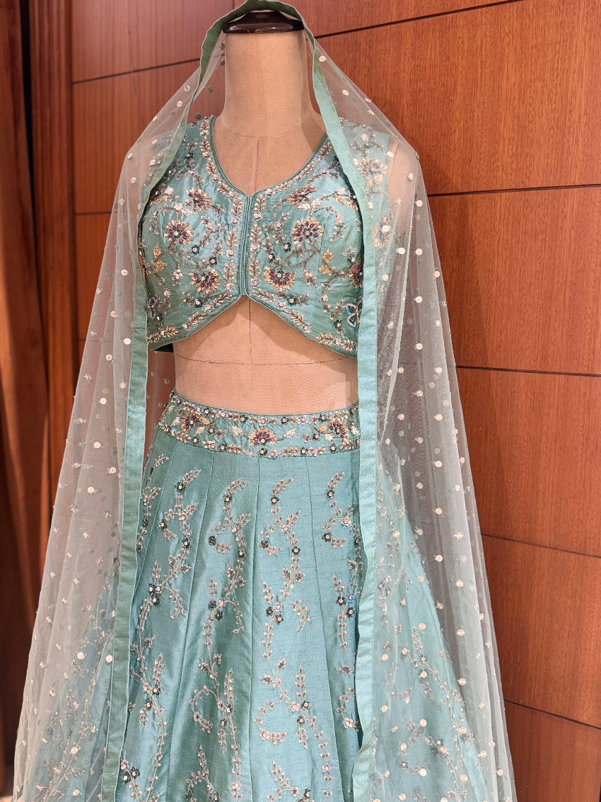 Teal embroidered lehenga with a sheer dupatta on a mannequin against a wooden background