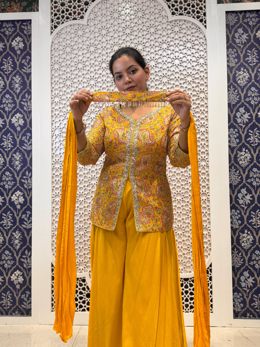Woman holding a yellow dupatta in front of a decorative wall.