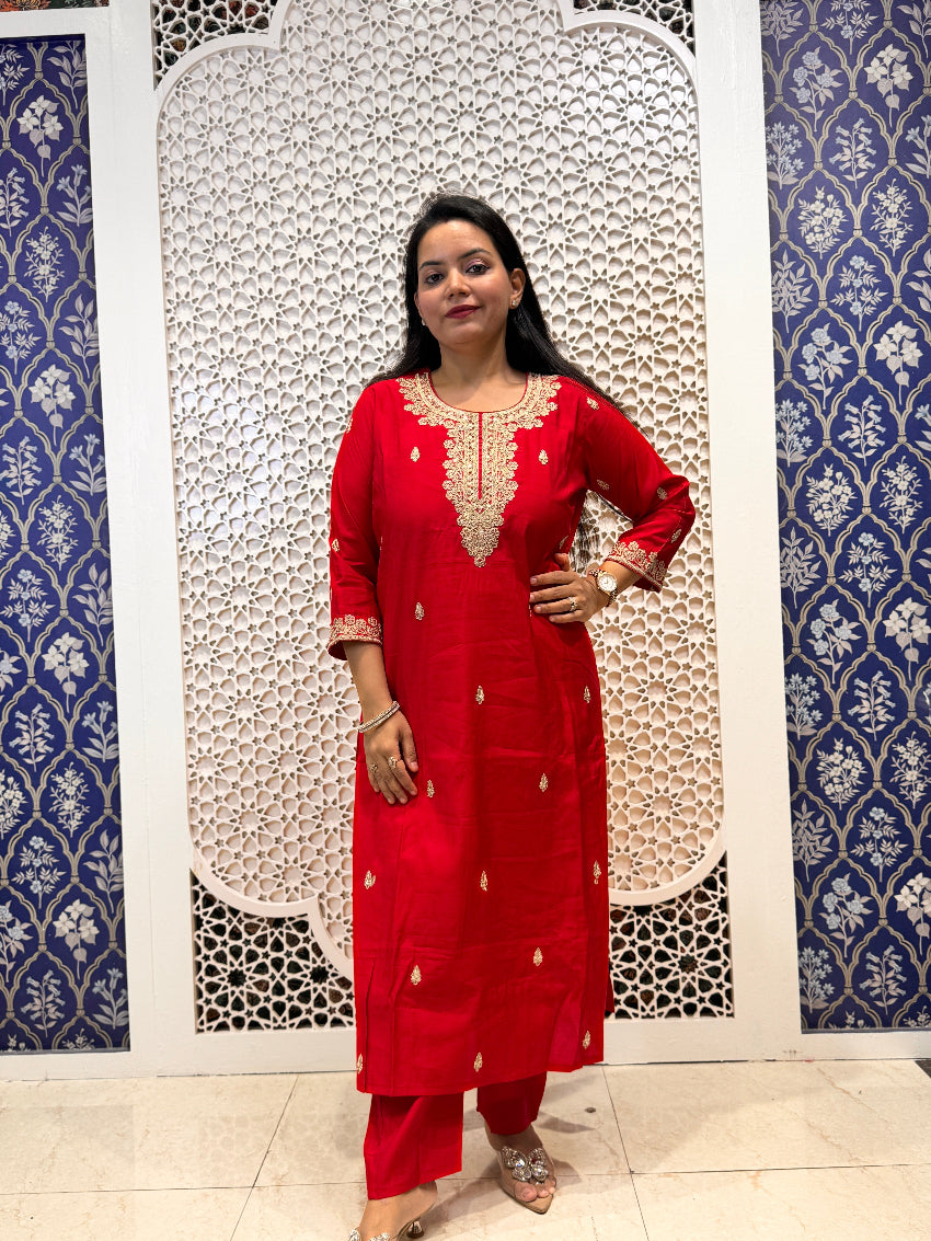 Woman in a red traditional outfit standing against a decorative wall.