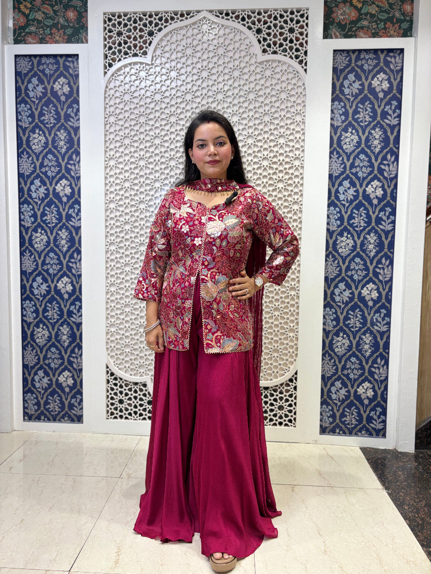 Woman in a pink traditional outfit standing in front of decorative wall panels.