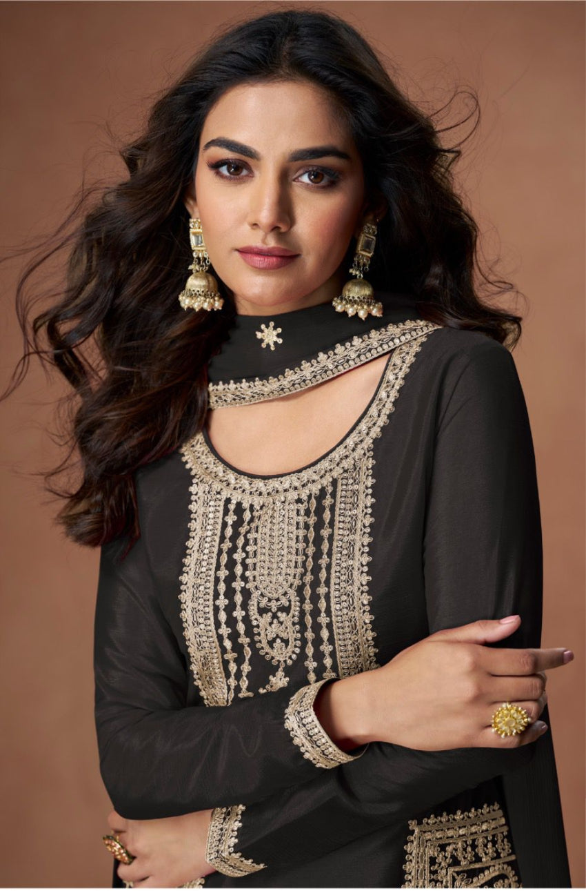 Woman wearing a black outfit with gold embroidery and jewelry against a brown background