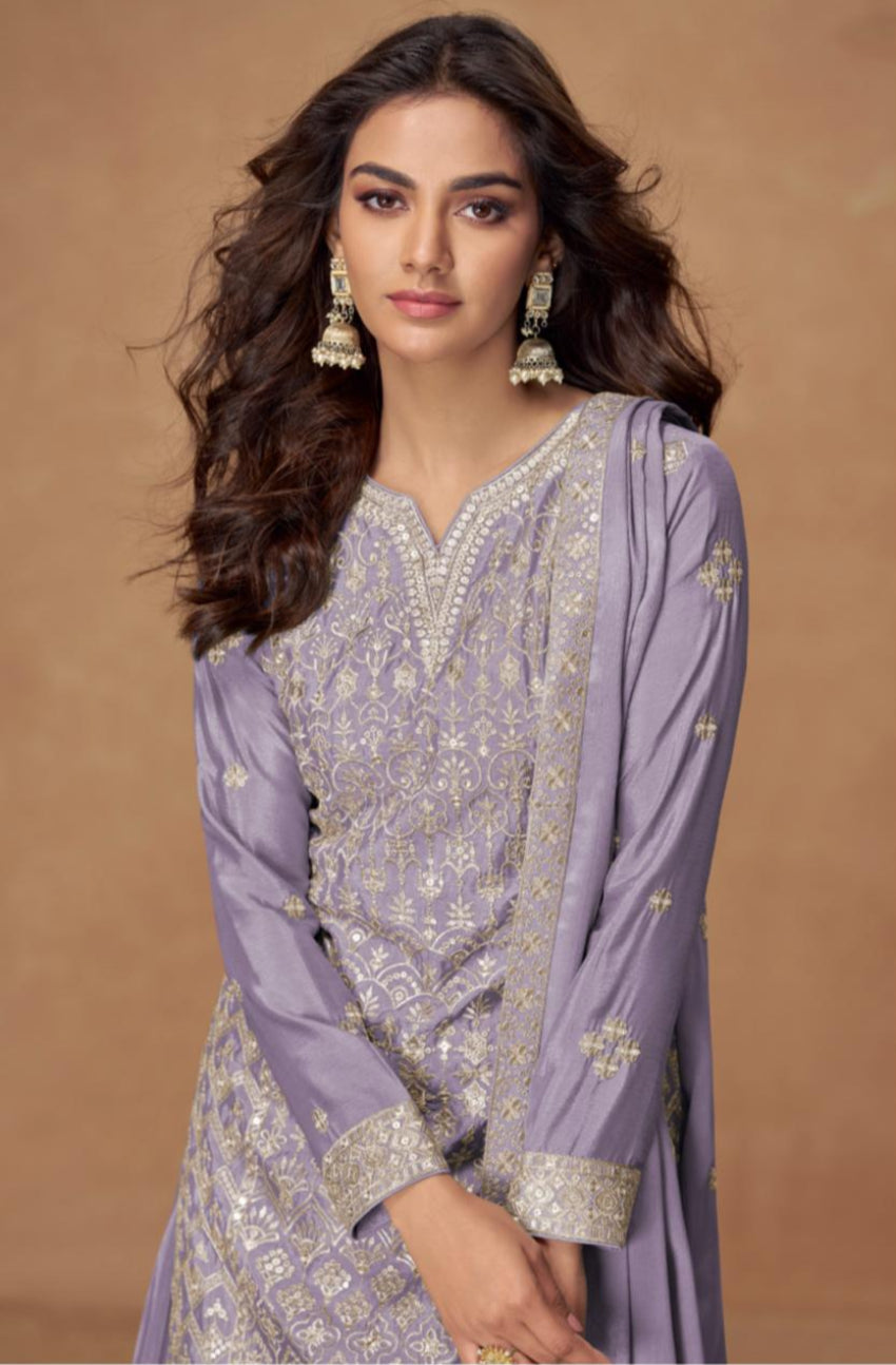 Woman wearing a light purple traditional outfit with intricate designs on a brown background