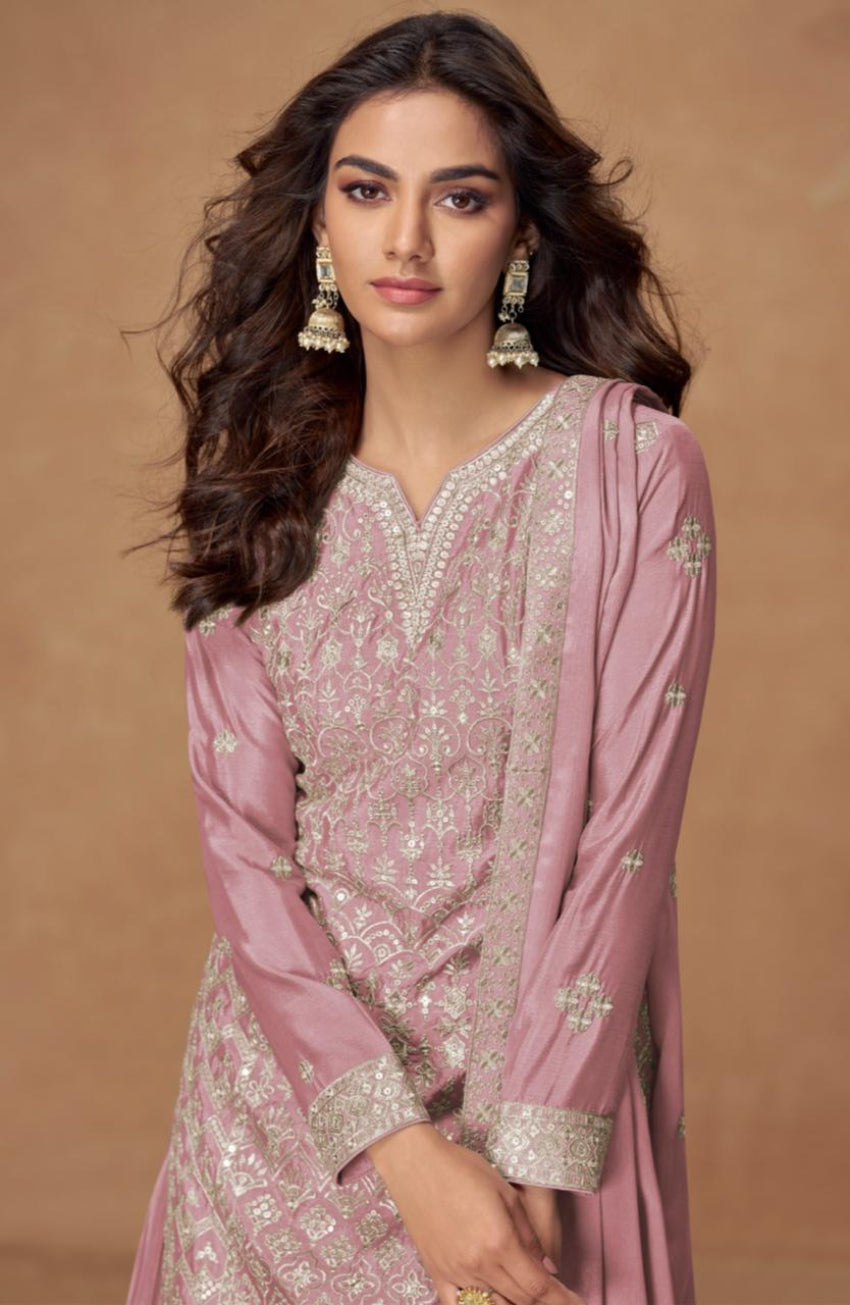 Woman wearing a pink traditional outfit with intricate patterns on a brown background