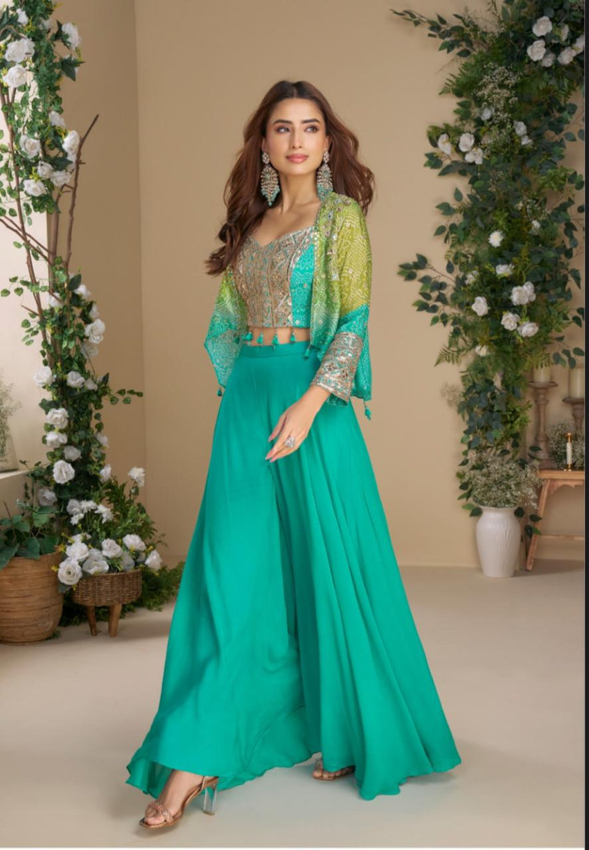Woman in a green and silver traditional outfit standing in a decorated room with flowers.
