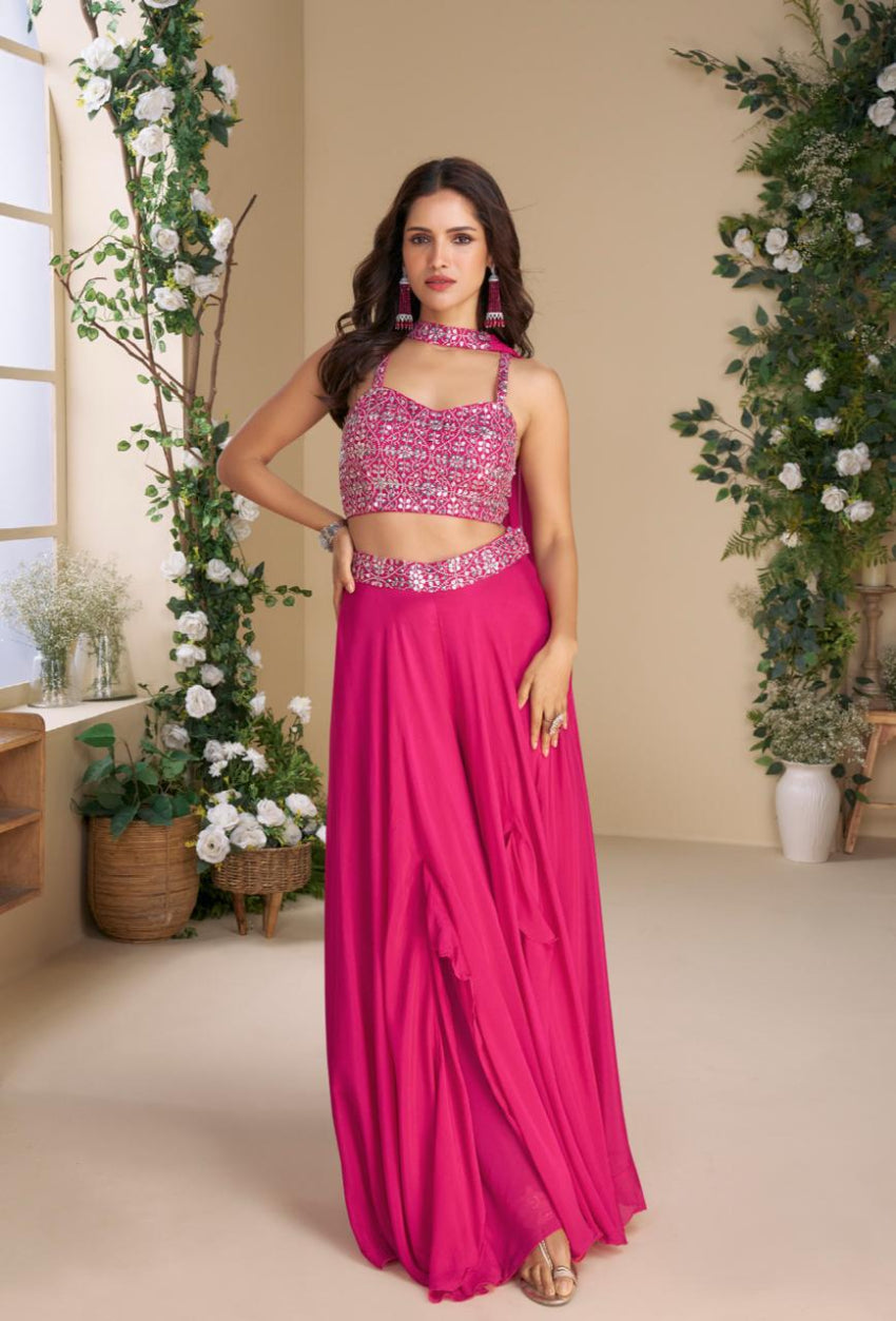 Woman in a pink saree with a matching blouse standing in a decorated room.