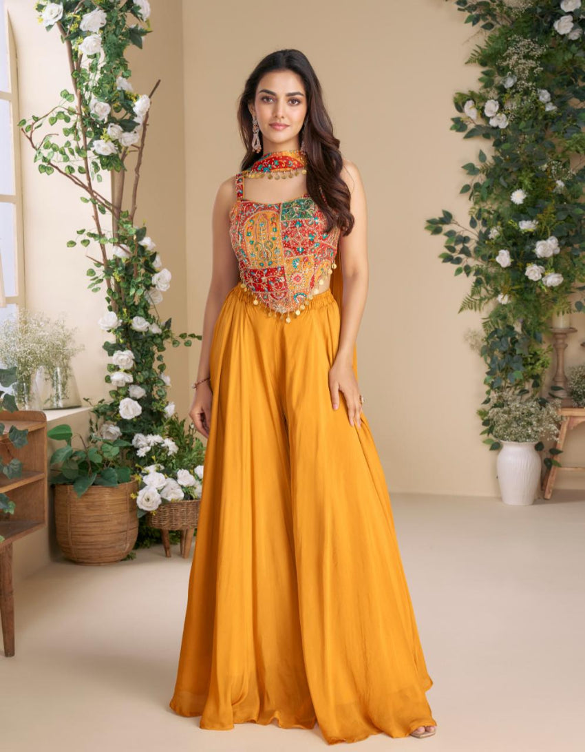 Woman in a colorful top and yellow skirt standing in a decorated room with plants.