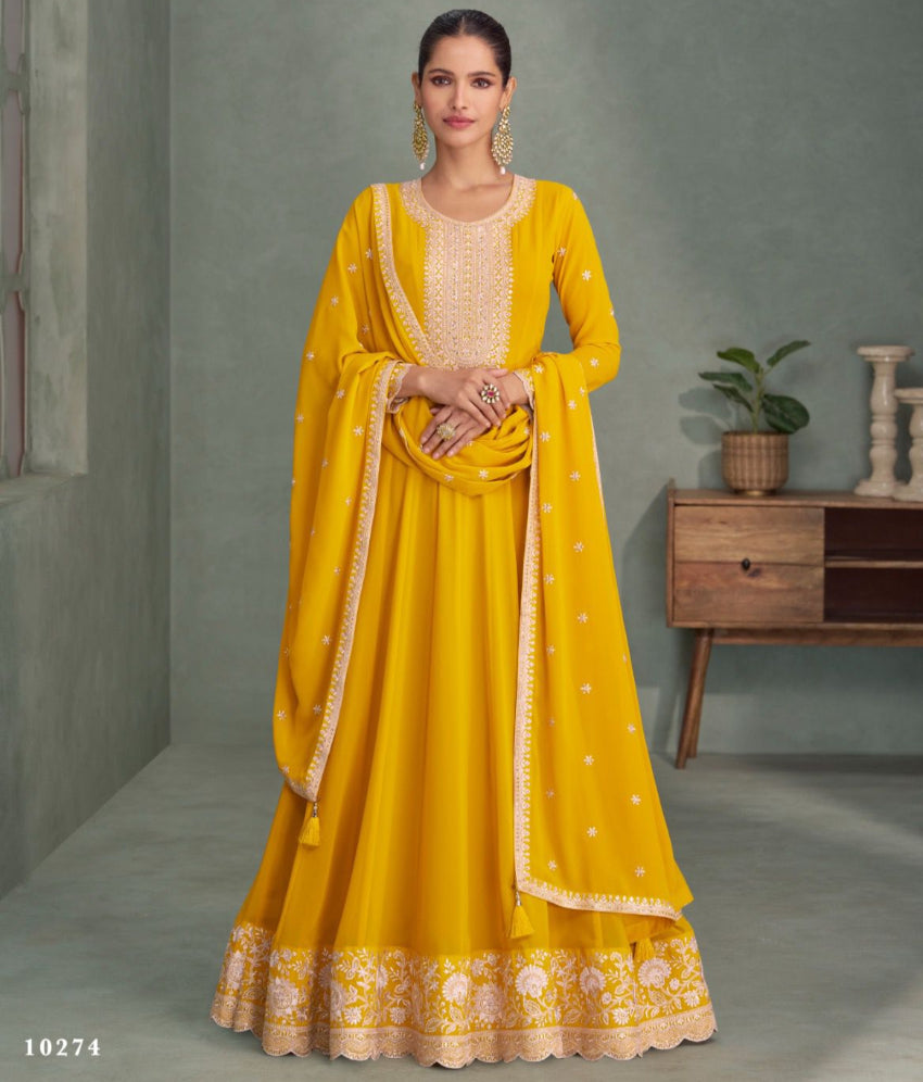 Woman wearing a yellow traditional outfit with gold embroidery in a room setting.