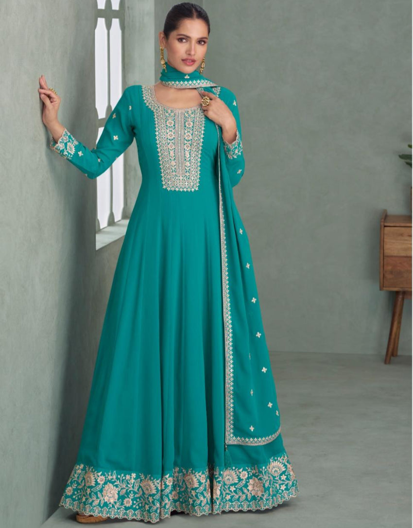 Woman wearing a teal embroidered dress against a gray wall.