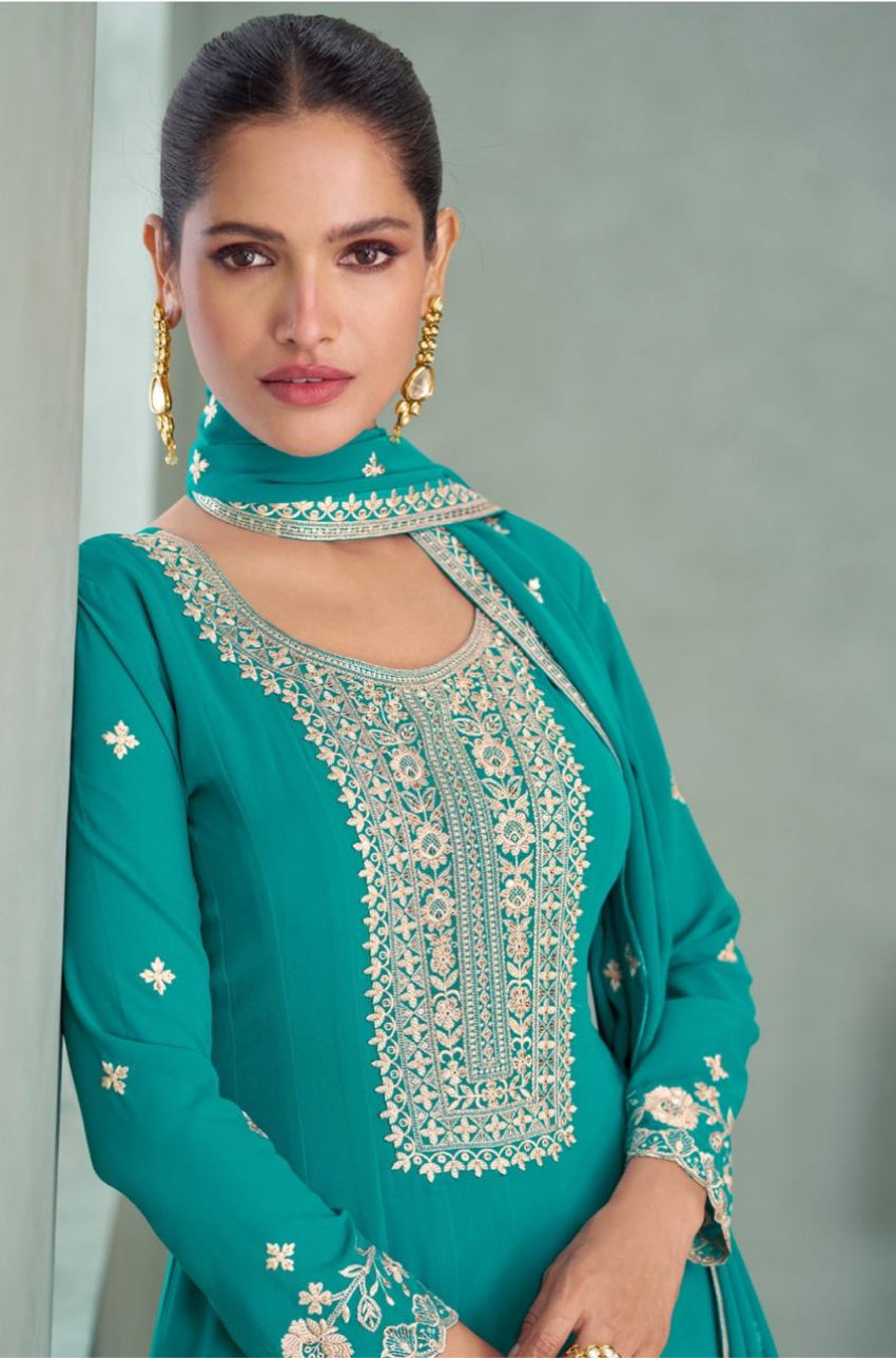 Woman wearing a teal embroidered traditional outfit against a gray background