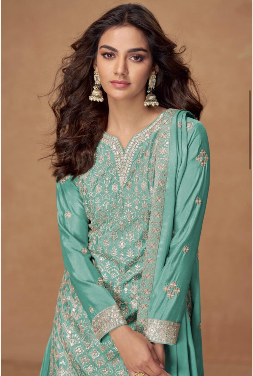 Woman wearing a green traditional outfit with intricate patterns on a brown background
