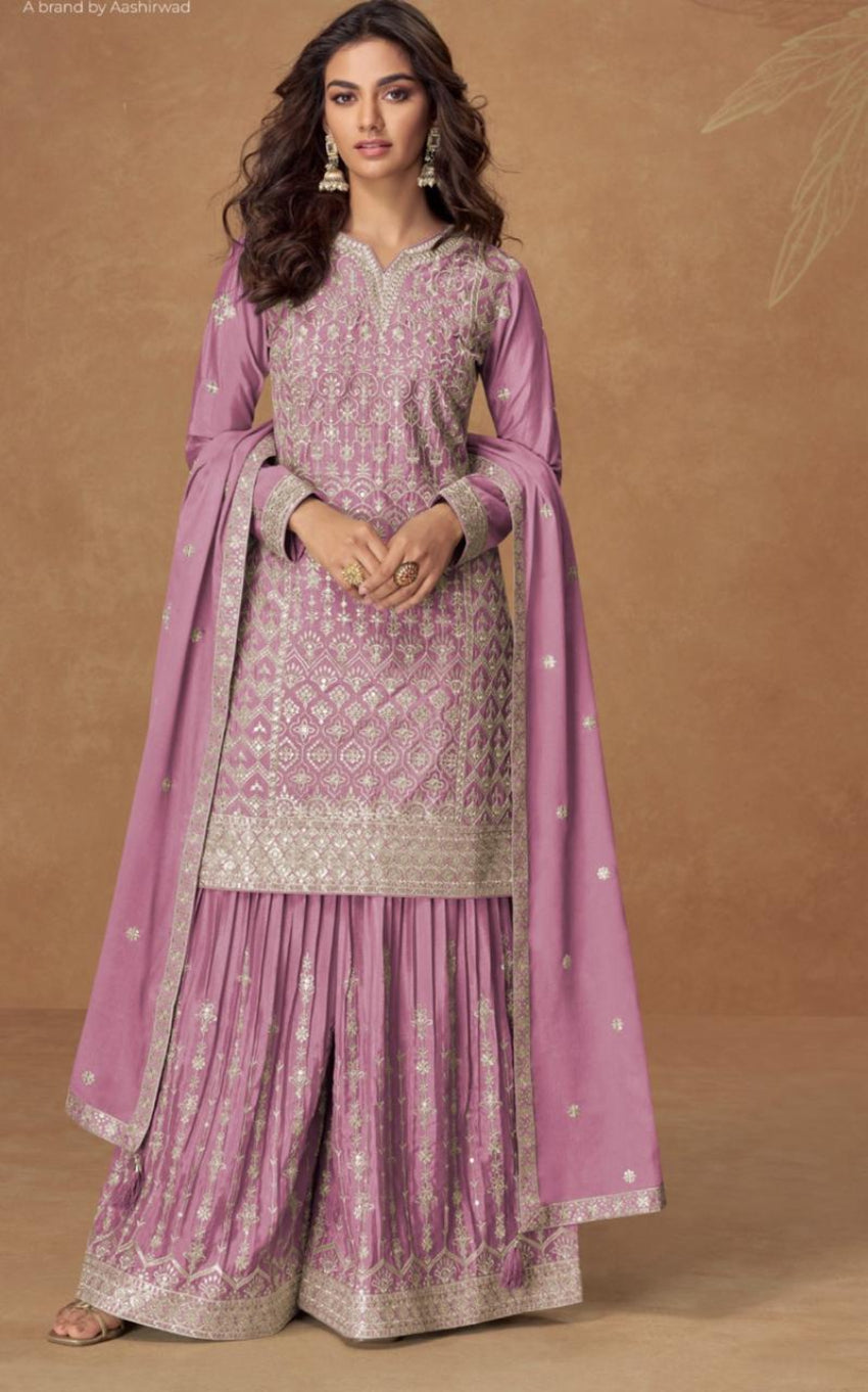 Woman wearing a pink and white traditional outfit with a matching dupatta on a brown background