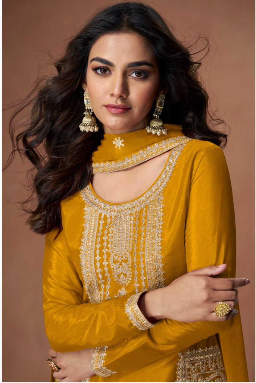 Woman wearing a mustard yellow traditional outfit with intricate designs on a brown background
