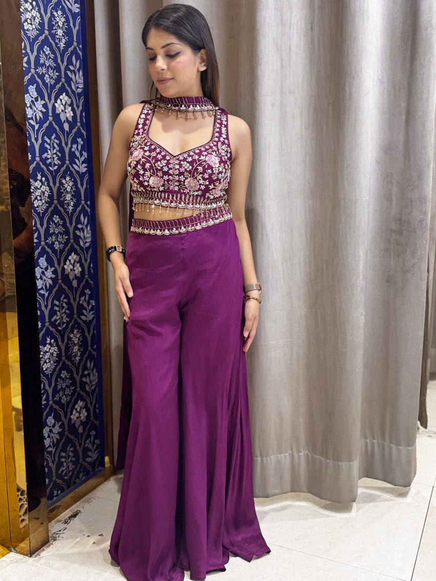 Woman wearing a purple outfit with a matching top and pants against a curtain background