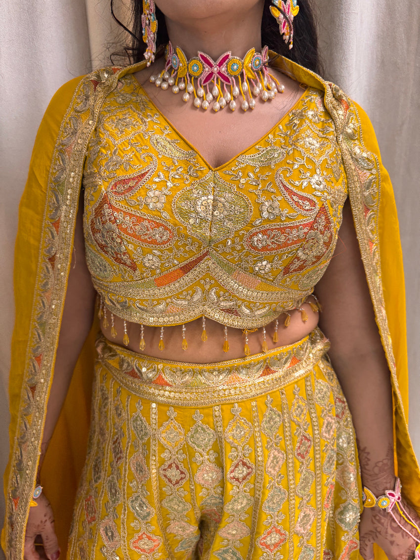 Close-up of a person wearing a yellow and gold embroidered traditional outfit with jewelry.