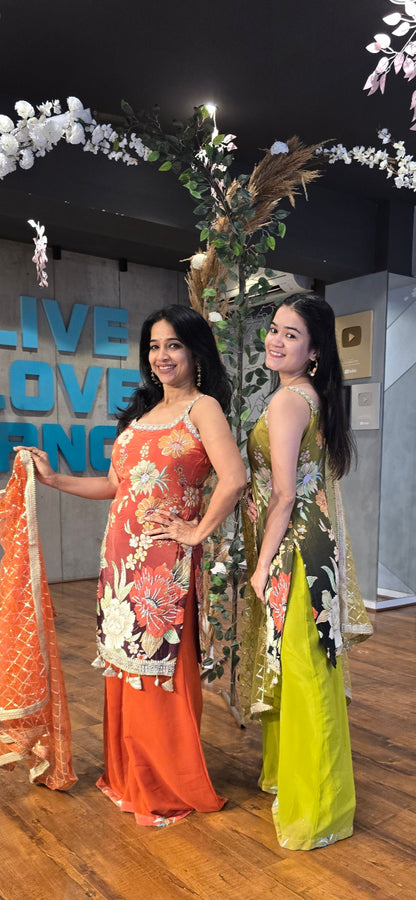 Two women in colorful traditional outfits standing on a stage with floral decorations.