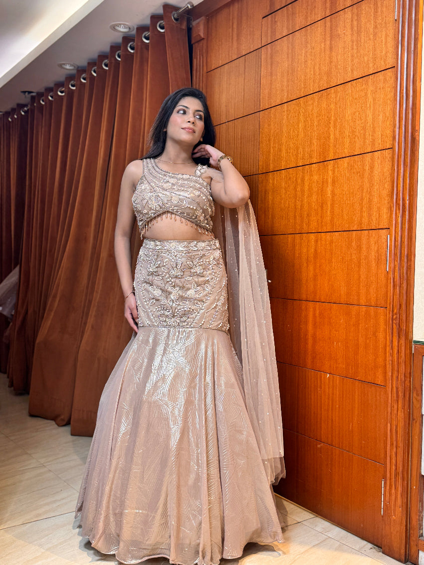 Woman in a beige and gold traditional outfit standing against a wooden door.