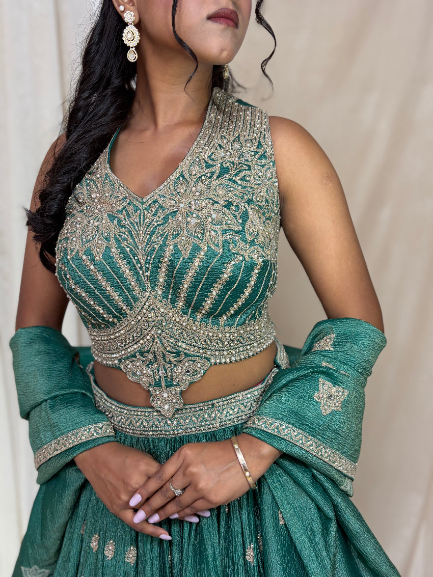Woman wearing a green and gold embroidered traditional outfit with a plain background
