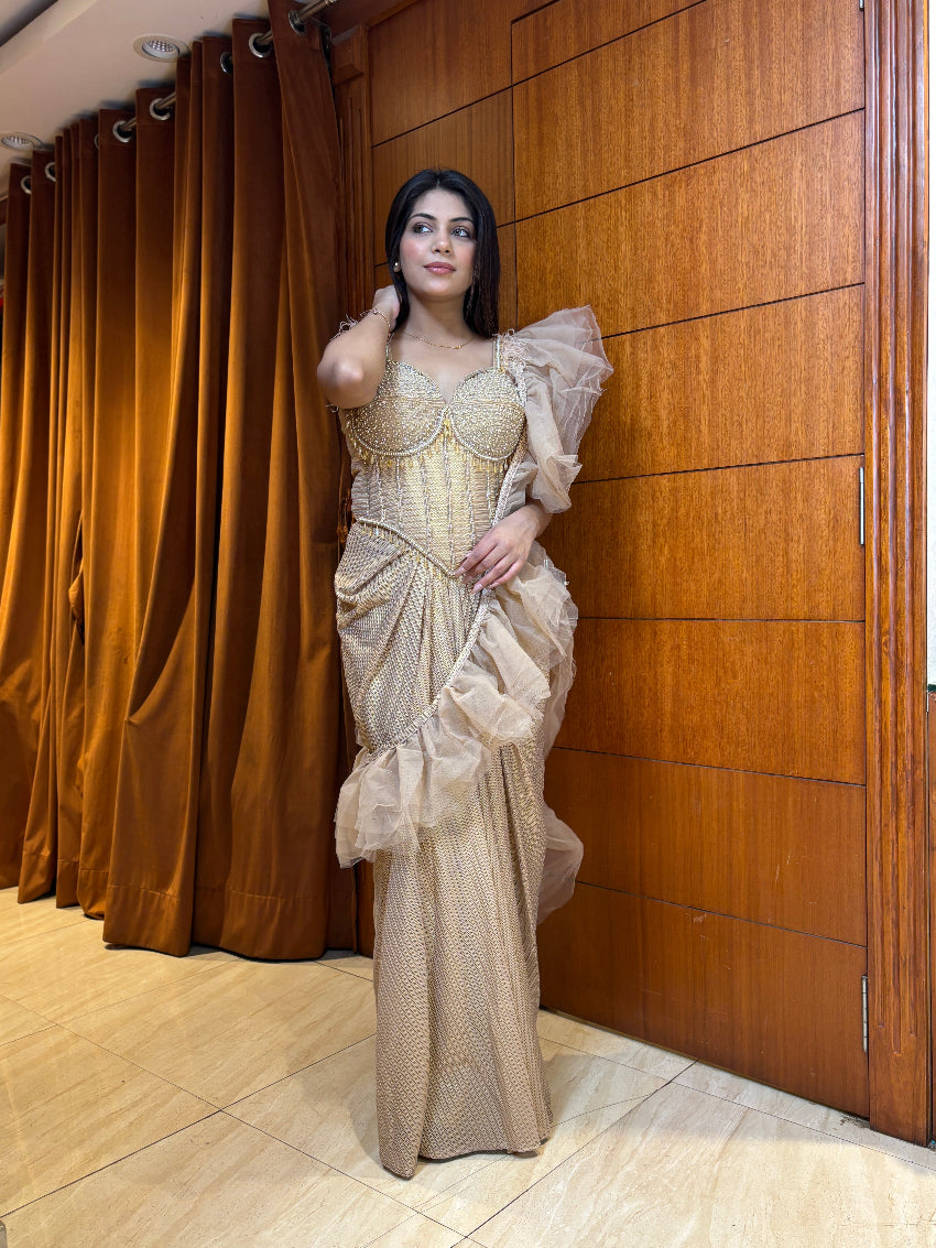 Woman in a beige evening gown standing against a wooden paneled wall.