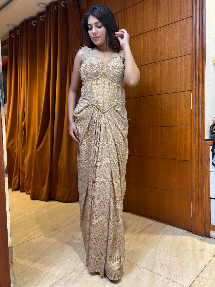 Woman in a beige evening gown standing in front of a wooden panel.
