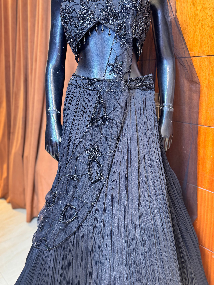 Elegant black evening gown with intricate detailing on a mannequin against a wooden background.