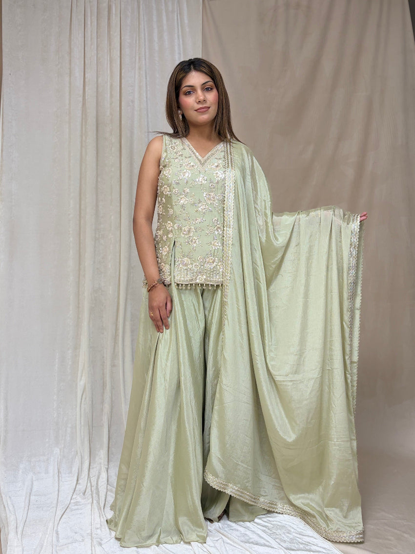 Woman wearing a light green traditional outfit with a dupatta against a plain background