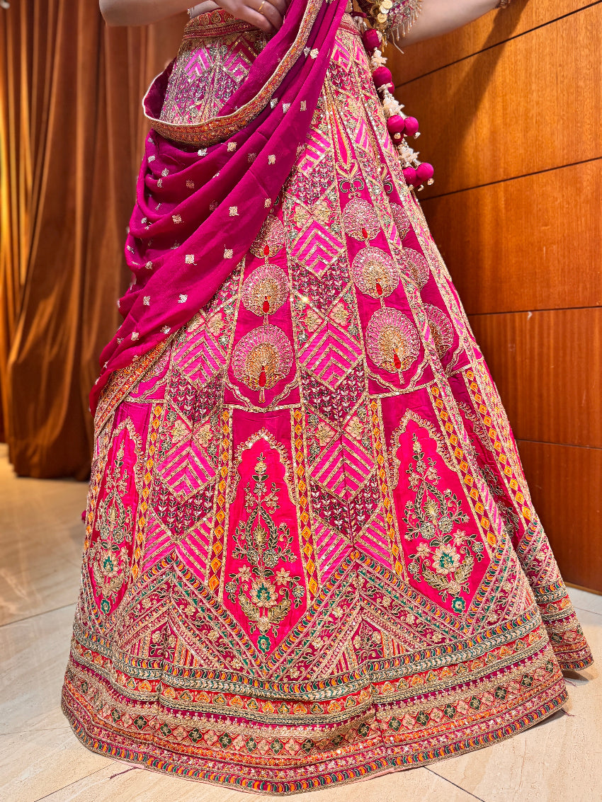 Traditional embroidered pink and multicolor lehenga with a matching dupatta against a wooden background.
