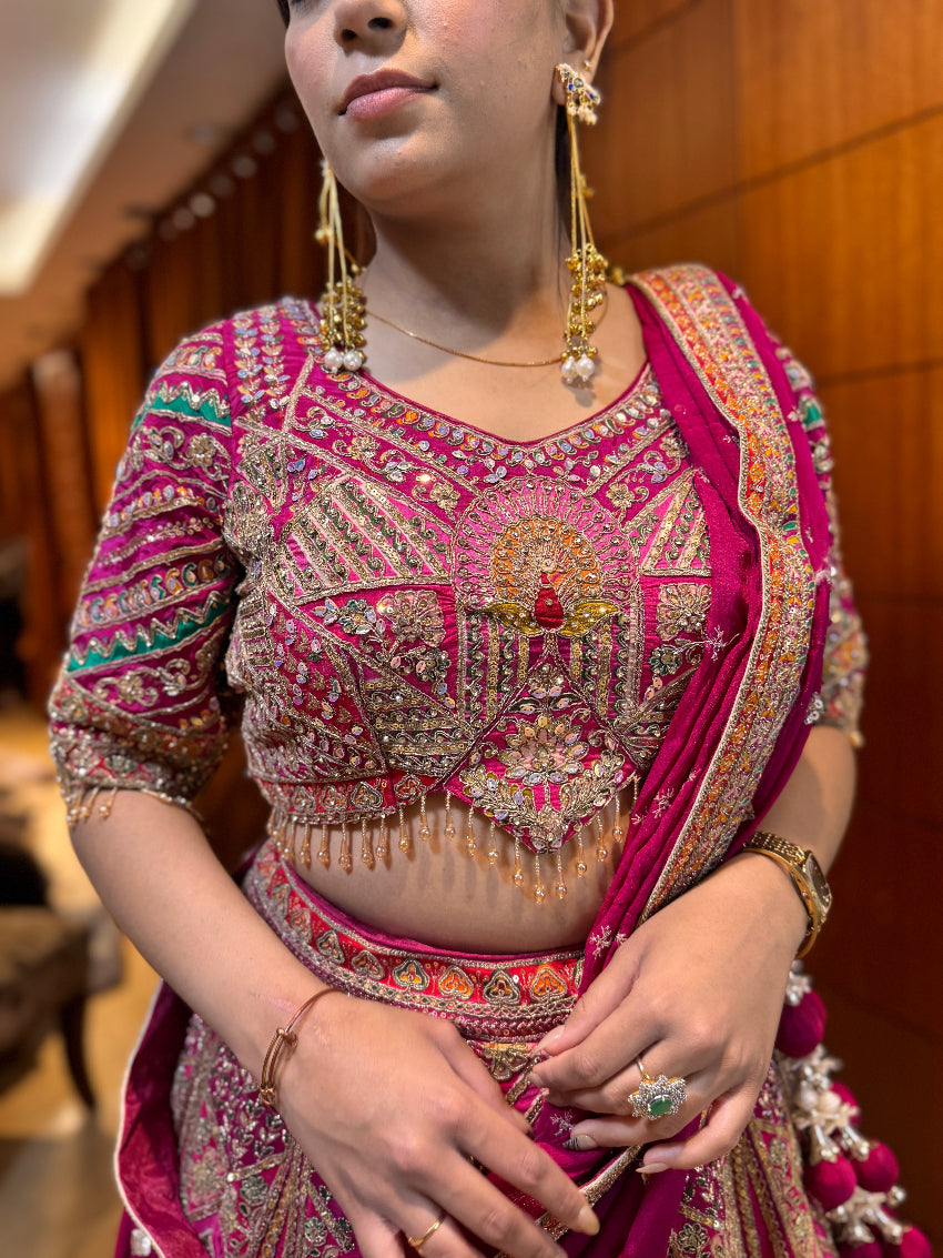 Woman wearing a traditional embroidered saree with gold jewelry indoors.