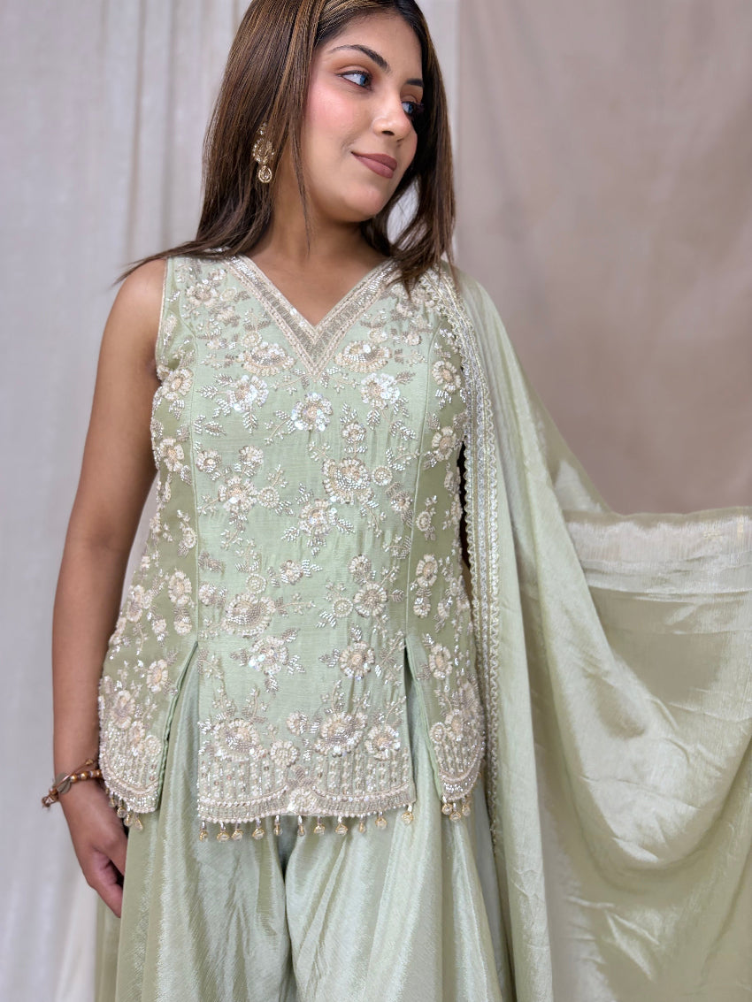 Woman wearing a light green embroidered outfit with a dupatta against a plain background