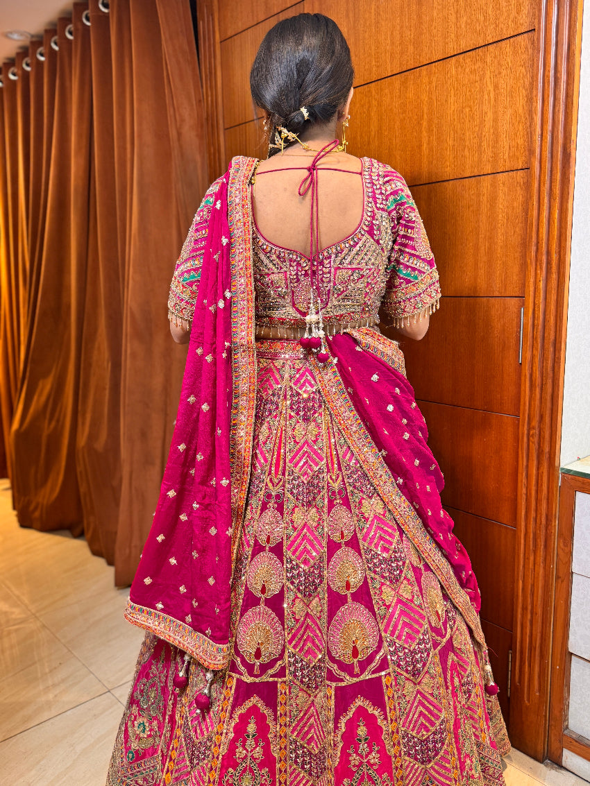 Woman in a traditional pink and gold embroidered outfit standing in front of a wooden door.