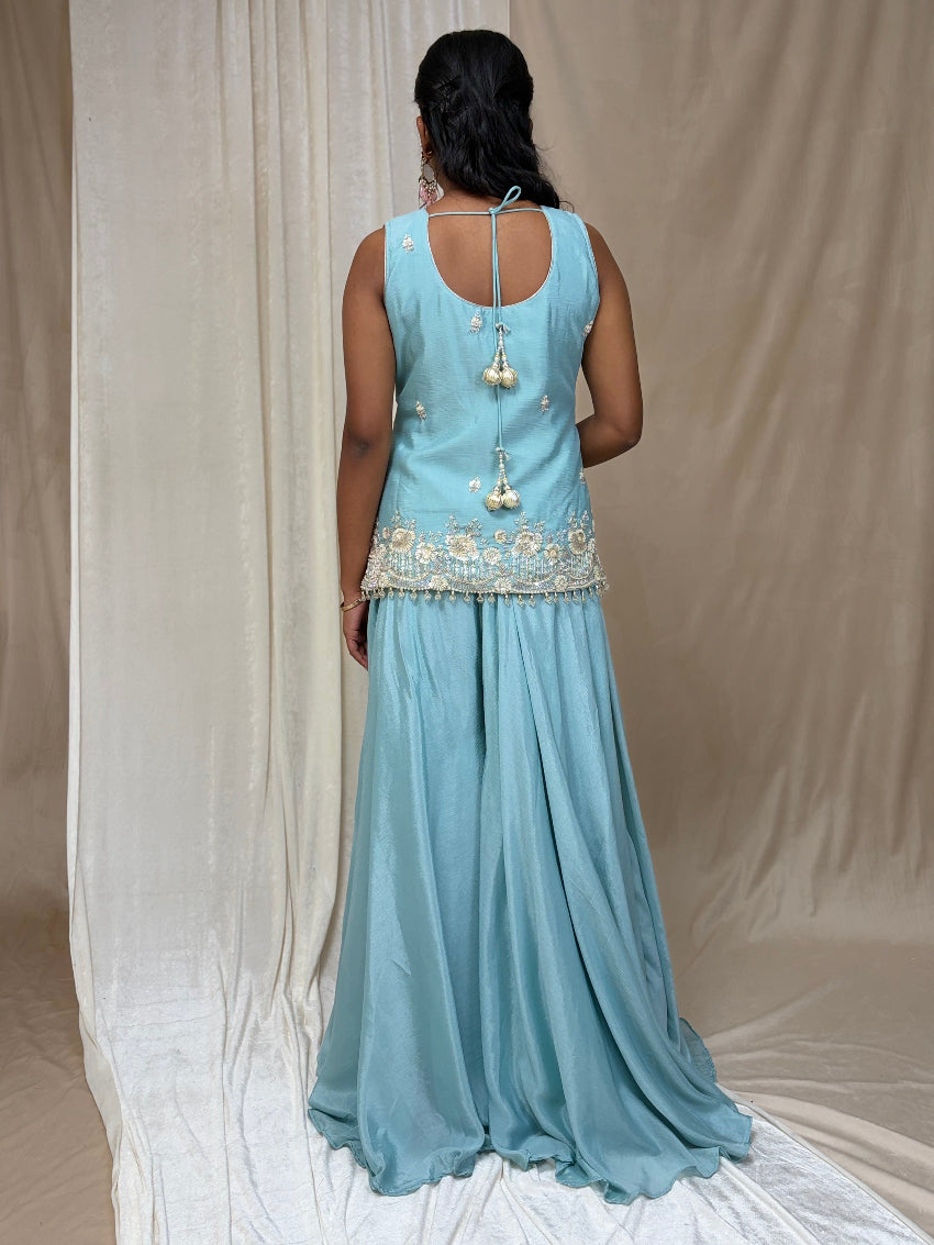 Woman wearing a light blue dress with floral embellishments against a beige curtain background