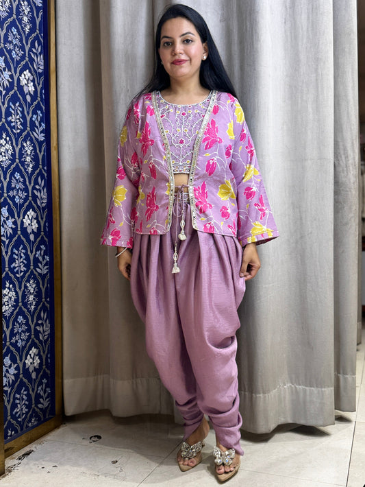 Woman wearing a traditional outfit with a floral top and purple pants in a decorated room.